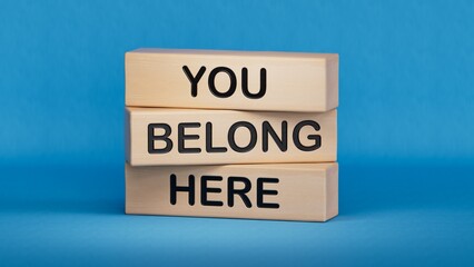 You belong here symbol. Wooden blocks with words You belong here.Business and You belong here concept. Wooden cube blocks. Copy space.3D rendering on blue background.