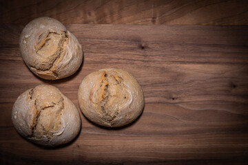 Drei selbstgebackene Brötchen auf dunklem Nussbaumholzbrettchen, Draufsicht