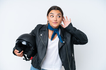 Young caucasian woman with a motorcycle helmet isolated on blue background listening to something by putting hand on the ear