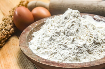 close-up of flour in a wooden bowl with eggs and rolling pin beside it.