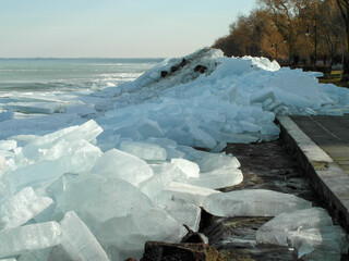 A frozen lake with large, fragmented sheets of ice scattered along the shoreline. 