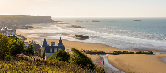 Panoramic view over Arromanches beach and Cap Manvieux in Normandy, France, at sunset with remains of the WWII artificial Mulberry harbour lying on the sand and in the sea.