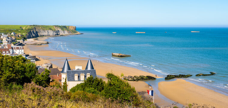 Panoramic view over Arromanches beach and Cap Manvieux in Normandy, France, on a sunny day, with remains of the WWII artificial Mulberry harbor lying on the sand and in the sea.