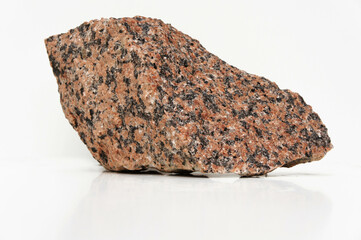 A reddish, speckled granite rock fragment with a coarse, rough texture, jagged edges, and a dense, durable structure, featuring black crystalline grains on its uneven surface.