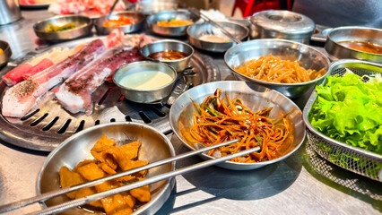Samgyeopsal grill setup with multiple side dishes in a Korean restaurant