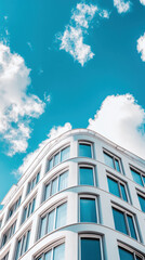 Fototapeta premium Modern architectural building with curved facade against bright blue sky with scattered clouds