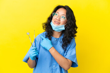 Young asian dentist holding tools over isolated background pointing to the side to present a product