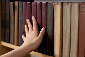 Female librarian hand putting a book on a bookshelf. Woman reader in the library taking a book from the shelf. Concept of library, reading, old classic literature
