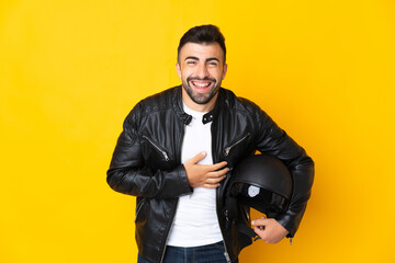 Caucasian man with a motorcycle helmet over isolated yellow background smiling a lot