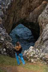 Chica rubia mirando cueva del mar en la costa de Asturias