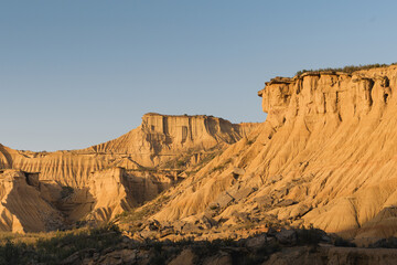Golden hour sunlight highlighting unique eroded sandstone formations in the bardenas reales desert landscape, navarra, spain