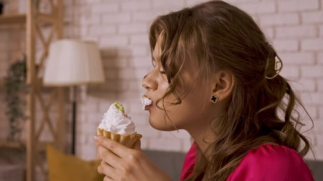 Young woman sitting at table and eating cake with whipped cream, taking a bite chewing, enjoying taste of sweet dessert snack, happy expression. Slow motion.