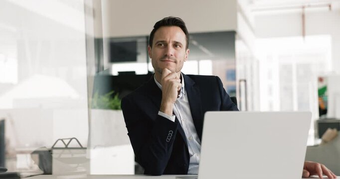 Thoughtful happy Latin businessman working at laptop in office, looking away with dreamy smile, thinking on creative ideas for project, planning business strategy, typing