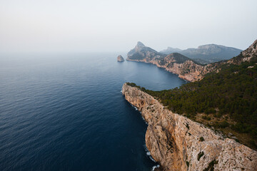 A magnificent view of Mallorca's rocky cliffs meeting the deep blue Mediterranean Sea. The coastline showcases the island's natural beauty, with lush greenery perched atop rugged cliffs