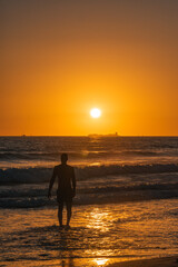 Silueta de un hombre en la orilla de la playa al atardecer con el sol de fondo