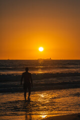 Fototapeta premium Silueta de un hombre en la orilla de la playa al atardecer con el sol de fondo