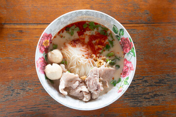 Above view of Tom Yum Noodles with Pork and Pork meatballs. Spicy Thai food that is easy to eat. Placed on a wooden floor.