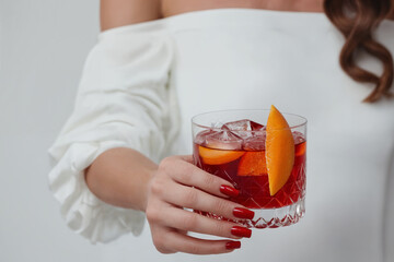 Close up of a female hands holding a glass of negroni cocktail on white background