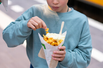 Boy eating french fries with mayonnaise on street food stall