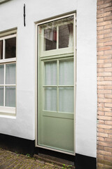 Puerta con ventana de cristal de color verde claro en fachada blanca