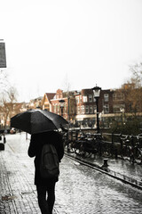 Persona caminando con paraguas negro mientras llueve por Ámsterdam