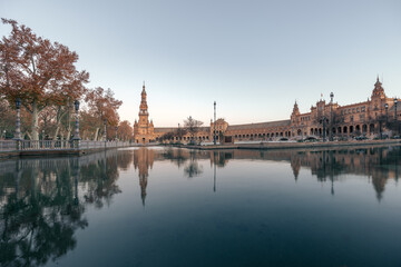 Plaza de España panoramic view with palace, tower and reflection in water at sunrise, Seville, Spain