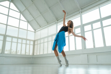 A woman performs a contemporary dance in a bright studio with large windows. Her pose highlights movement and flexibility, making it ideal for themes of fitness, dance, or lifestyle imagery.