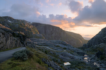 Norwegian mountain landscape at sunset, featuring rugged rocky terrain, winding roads.