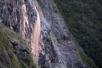 Tall waterfall cascading down a steep, rocky cliff surrounded by lush greenery.