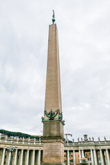 A tall column building with a statue on top in Vatican. The building is in a city