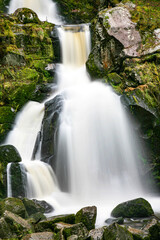 Fototapeta premium A waterfall in Triberg black forest with a misty spray. The water is white and the rocks are grey. The waterfall is surrounded by moss and rocks