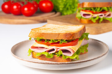 Close-up of two sandwiches with bacon, salami, prosciutto and fresh vegetables on rustic wooden cutting board. Club sandwich concept