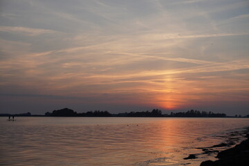 Stunning Sunset Over a Calm Lake with a Fiery Reflection in the Sky and Gentle Waves Touching the Shore – A Serene and Picturesque Evening Landscape Perfect for Nature and Travel Enthusiasts