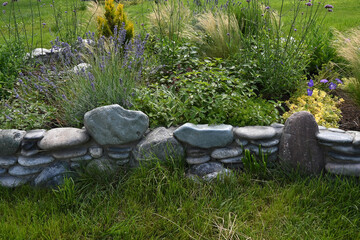 Charming flower bed in the garden is lined with stones with flowering and green plants. Colorful vegetation