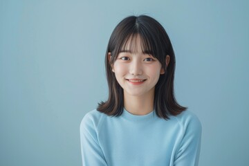soft features long hair, smiles gently woman while wearing blue shirt against simple plain background. Her relaxed posture calm expression convey sense of ease natural beauty.
