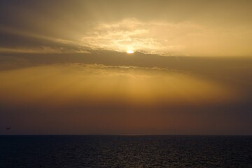 Obraz premium The sun shines brilliantly through clouds above the ocean at sunset
