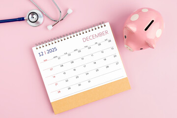 December 2025 desk calendar and stethoscope with piggy bank, Savings for Health insurance.