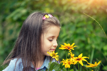 Naklejka premium Happy little girl sniffs flowers in the park on a sunny day