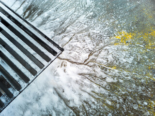 Soap sud waste flows to floor drain grid in car washing garage, close-up.