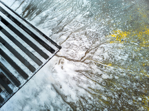 Soap sud waste flows to floor drain grid in car washing garage, close-up.