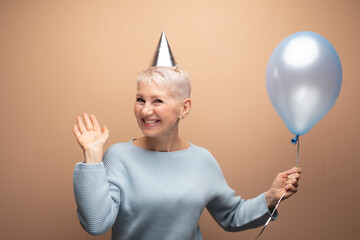 Portrait of gray-haired lady holding blue balloon having fun isolated on white beige color background