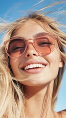 Smiling woman with blonde hair enjoying a sunny day outdoors while wearing stylish sunglasses and exuding happiness in a clear blue sky