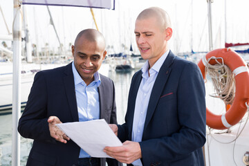 Two men in suits buy and sell a yacht in the seaport