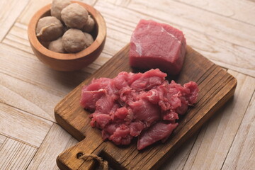 beef meatballs in a wooden bowl and raw beef. teakwood cutting board