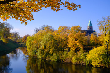 Fototapeta premium A river with green trees and a quaint church in the background