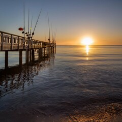 Obraz premium A serene fishing pier at dawn, with fishing rods leaning against the railing, and the first light of the sun reflecting on the water.