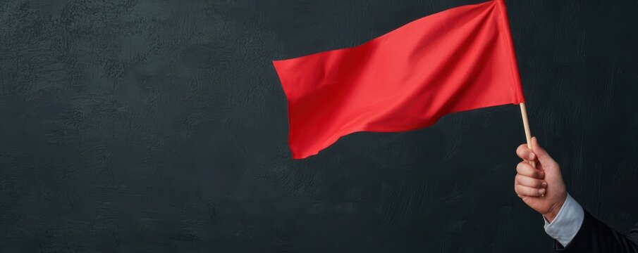 A hand holding a vibrant red flag against a dark background, symbolizing warning or alertness.