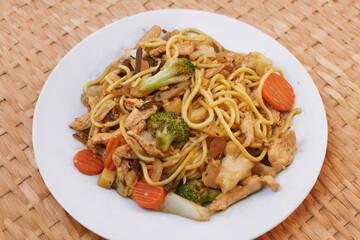 Oriental dish: Asian noodles with vegetables and chicken on a plate stands on the table.