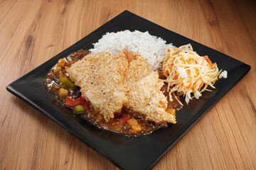 Oriental dish: crispy panko-coated chicken with vegetables, salad and rice on a plate stands on the table.