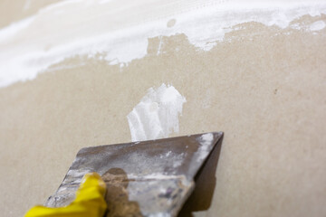 Preparing drywall for plastering. The craftsman cleans and sands the putty from the joints and screws with a spatula